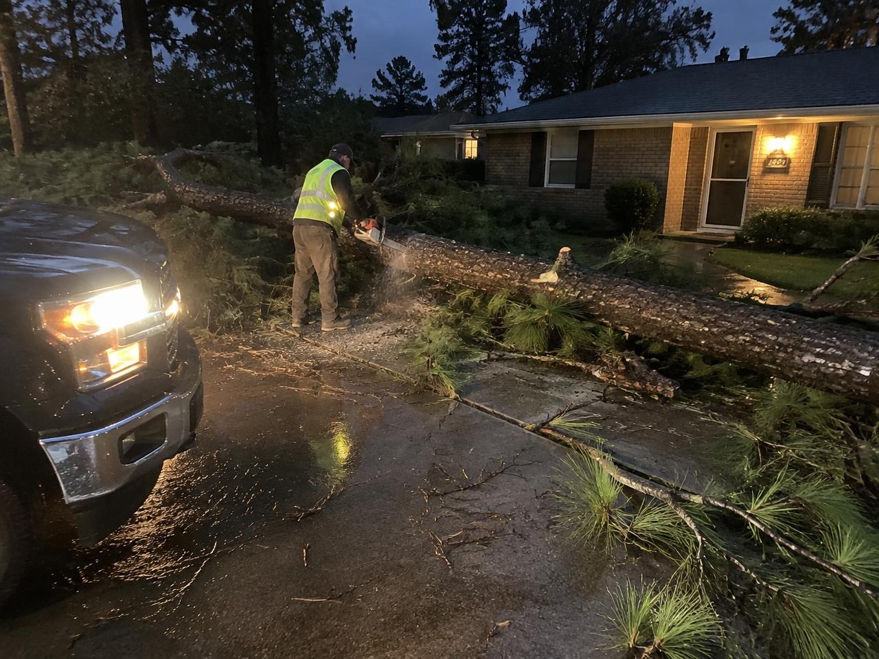Crew member cutting a fallen pine off a driveway at night after a storm in Apex, NC