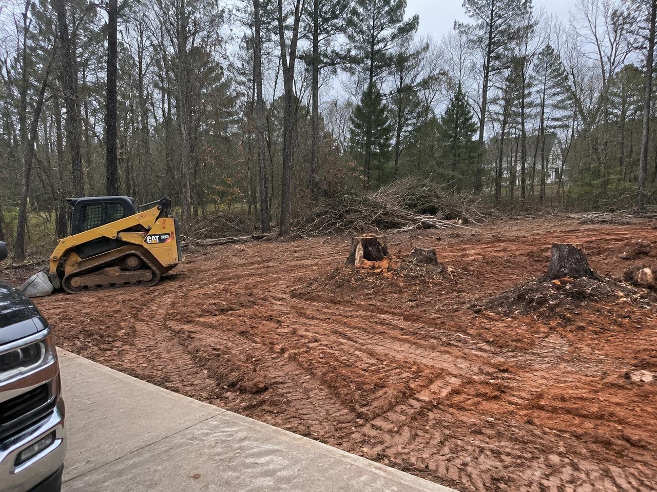 Partially cleared wooded lot in Wake County, NC with brush piles and a skid steer
